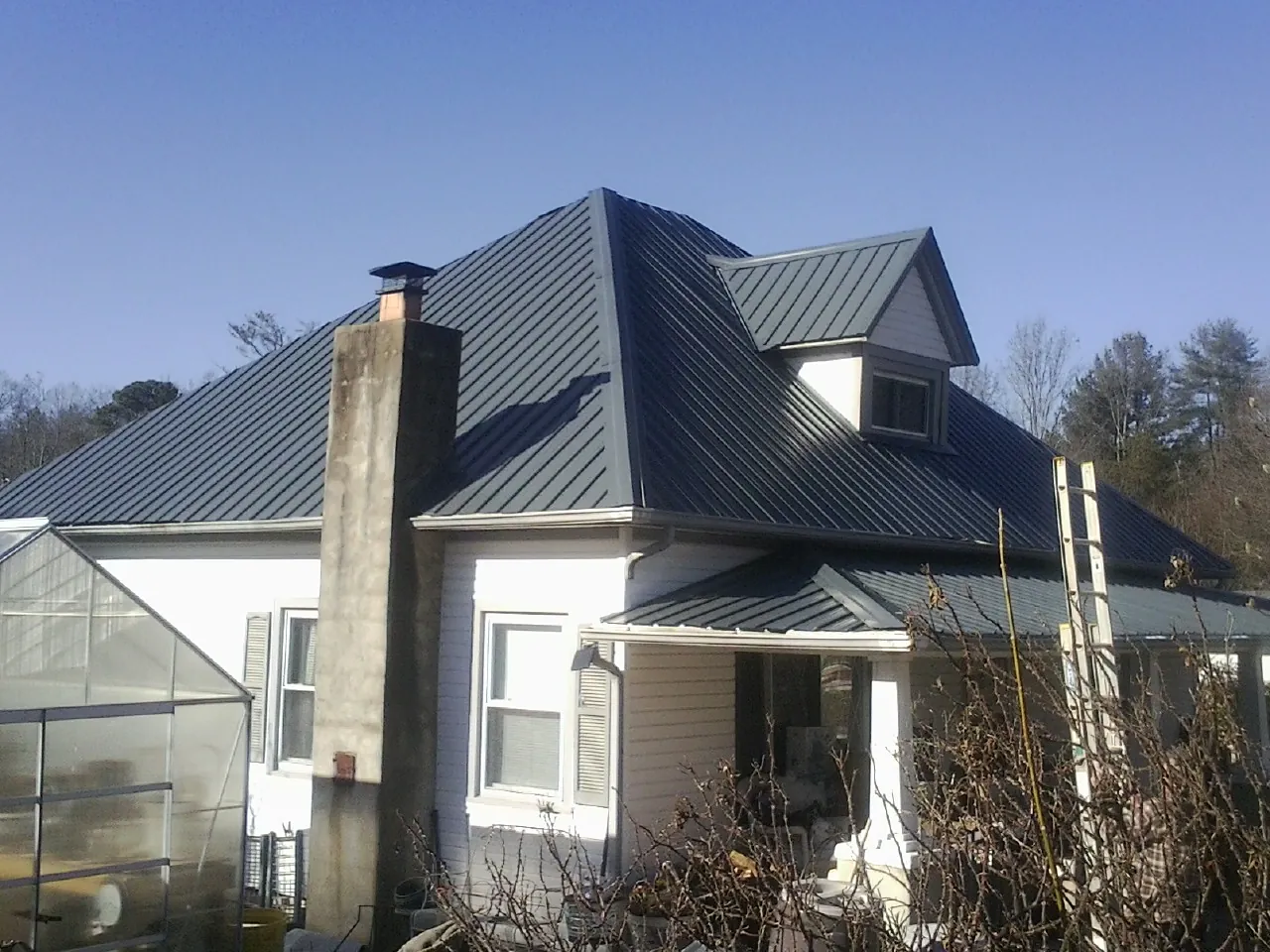 Dark blue standing seam metal roof on a white farmhouse with dormer — Slate & Tile Roof Repair by Roofing Brothers in Horseshoe Bay