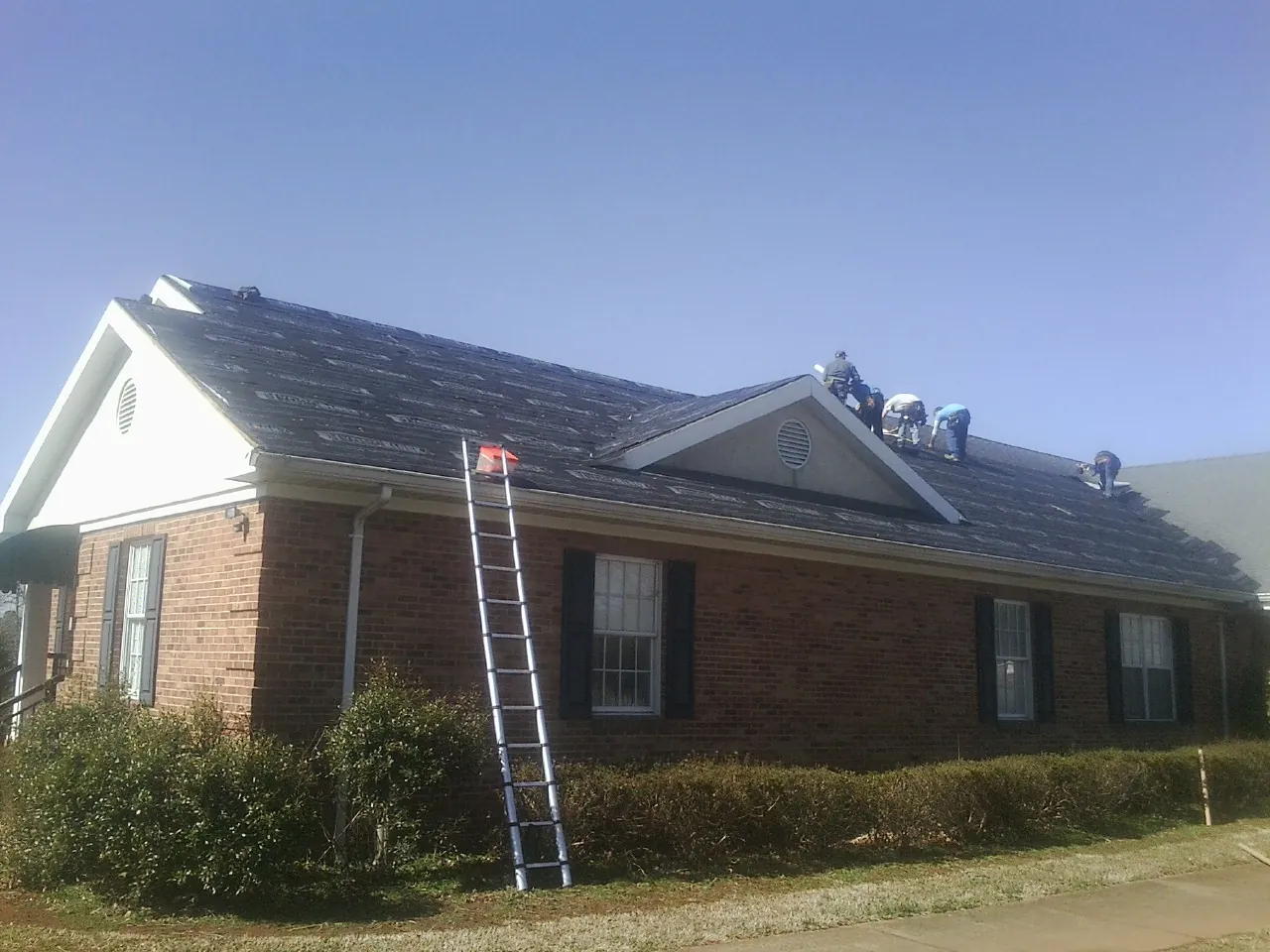 Crew tearing shingles off a brick ranch roof with a ladder set — Emergency Roof Repair work by our crew in Horseshoe Bay