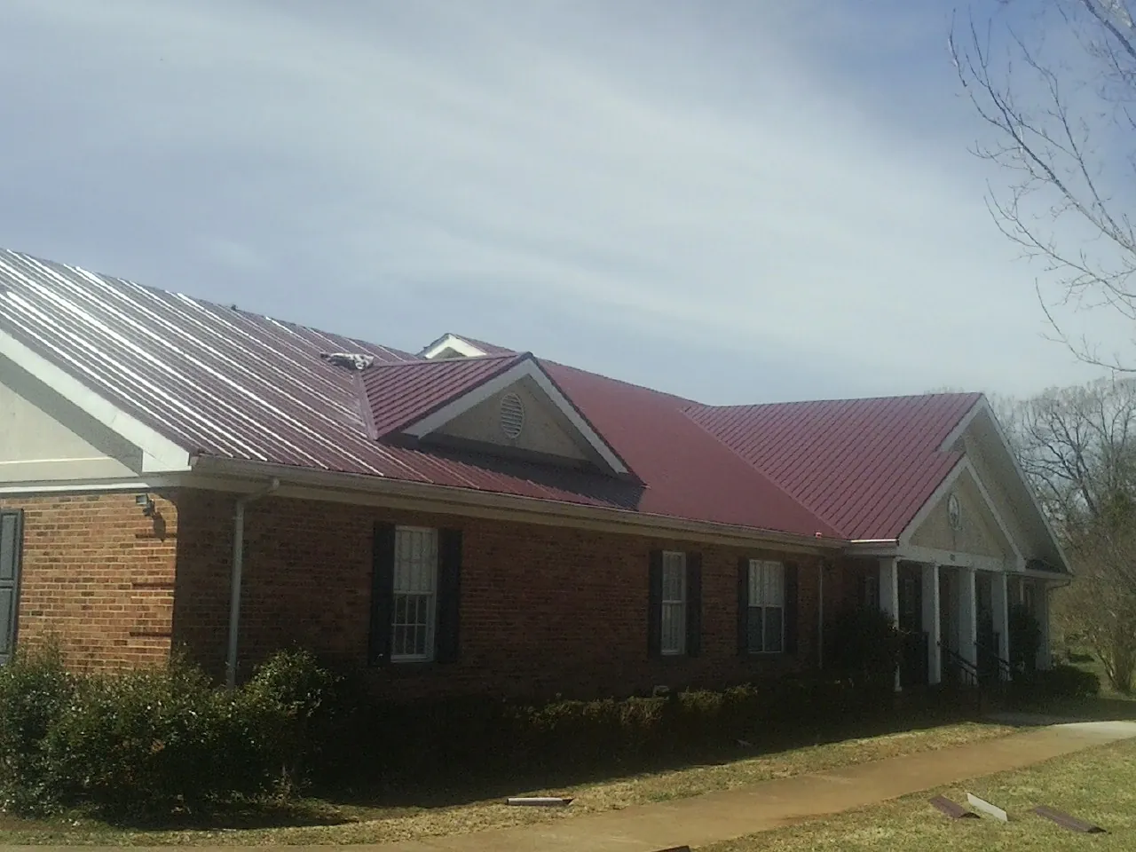 Red metal roof with gabled entries on a long brick building, from a Hail Damage Roof Repair job in Horseshoe Bay