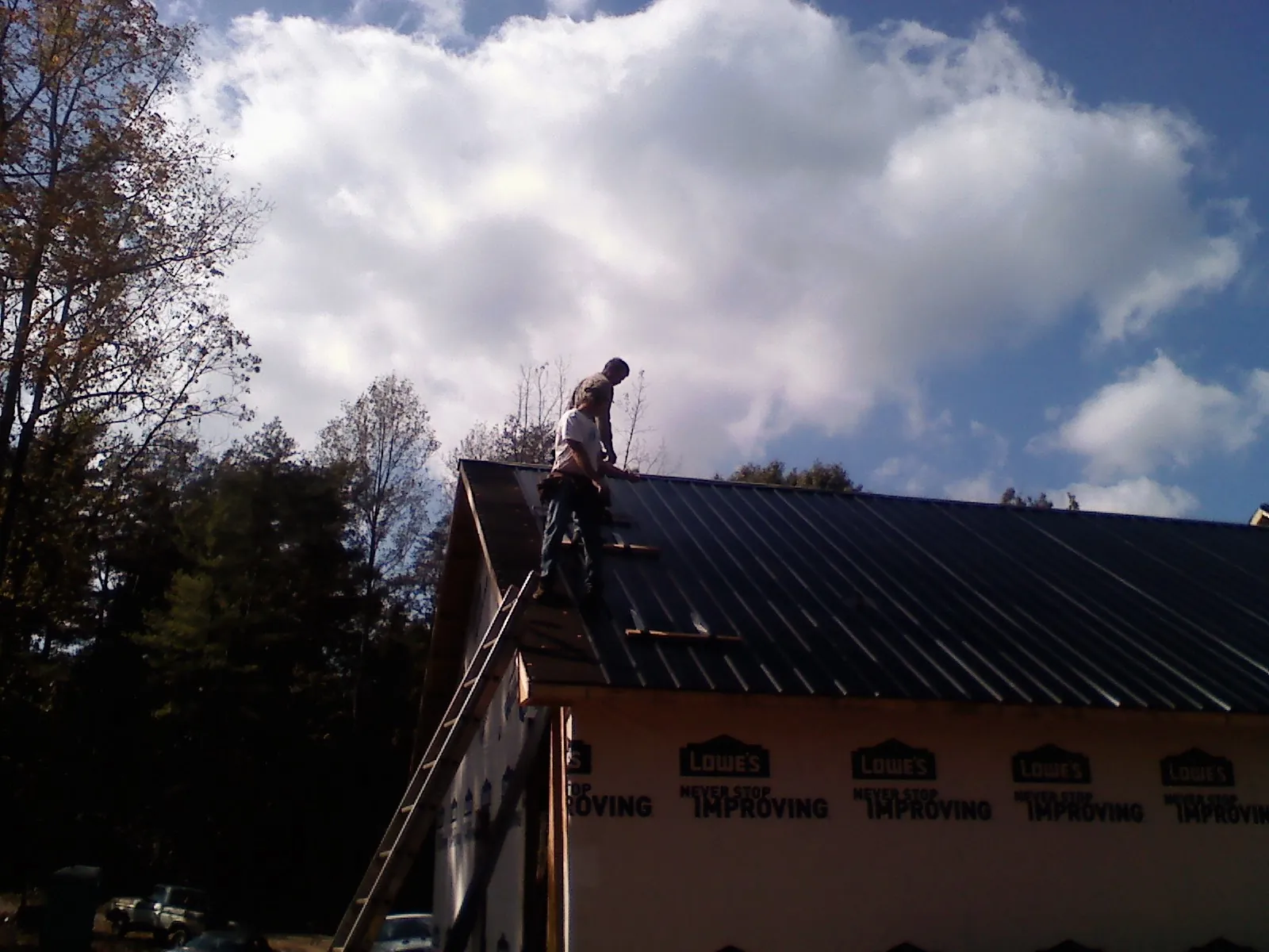 Roofer fastening dark metal panels high against a cloudy sky, from a Roof Inspection job in Horseshoe Bay