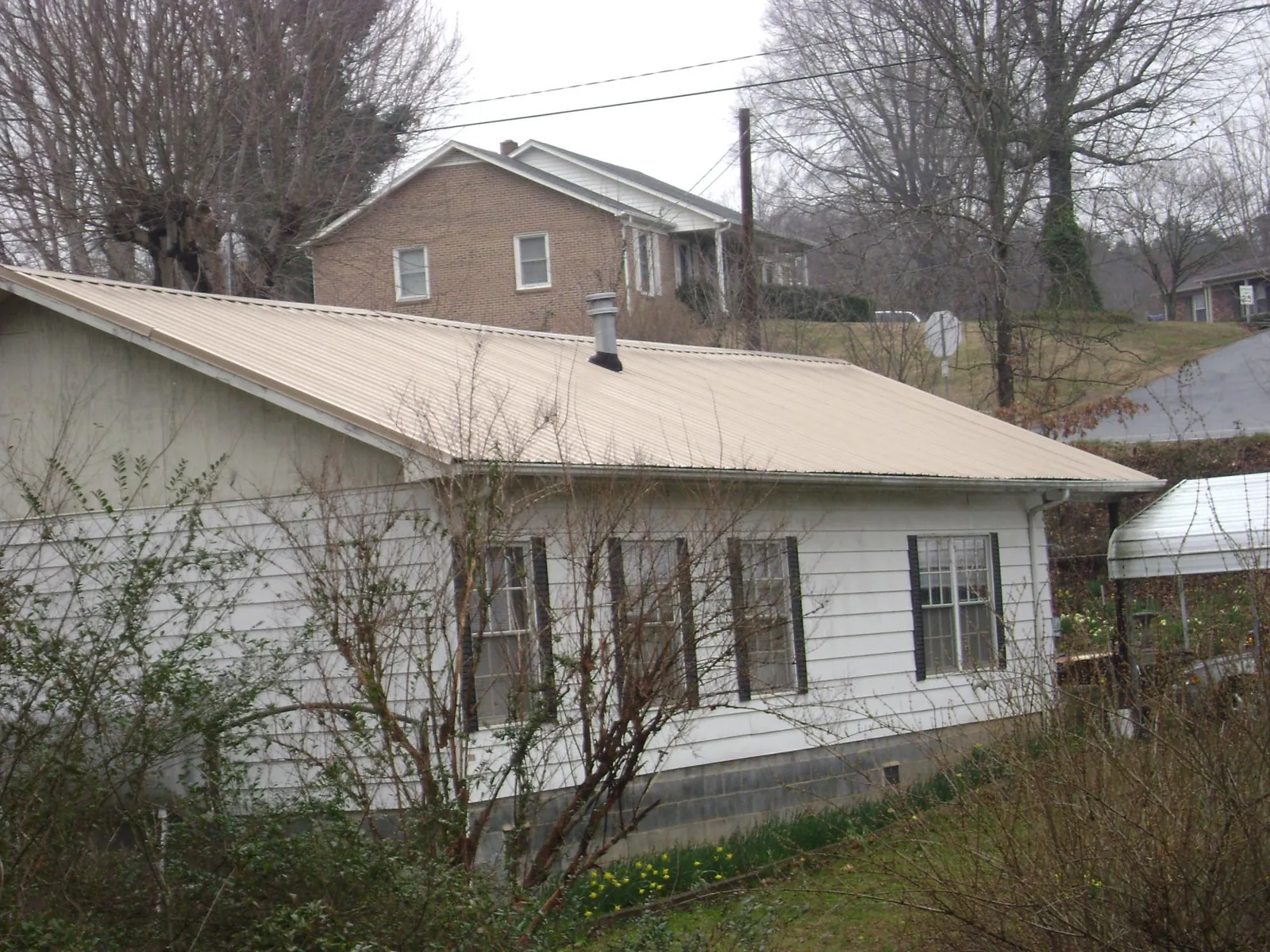 Tan metal roof on a white sided house set into a hillside — Commercial Roofing by Roofing Brothers in Horseshoe Bay