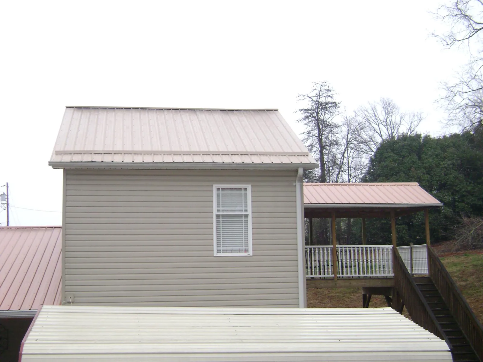 Tan metal roofs on a two story addition and attached porch, from a Roof Replacement job in Horseshoe Bay